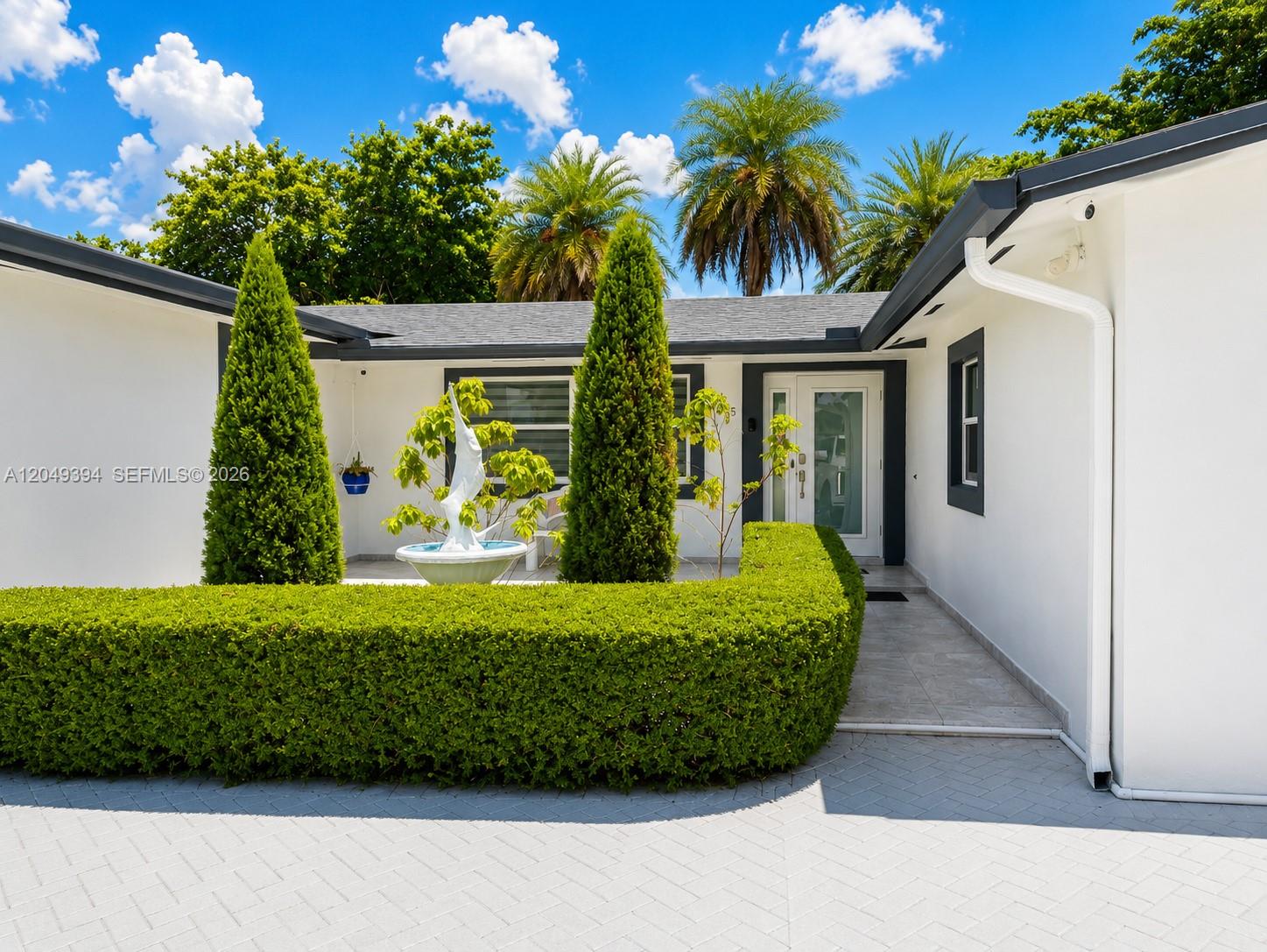 The exterior of a white house features a manicured hedge, two tall trees, and a fountain — 9675 SW 19th St, Miami FL 33165, MIAMI, FL