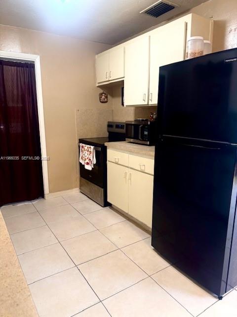 A kitchen features white cabinets, a black refrigerator, a stainless steel stove, and tiled floors — 1481 SW 7th Ter, Deerfield Beach FL 33441, DEERFIELD BEACH, FL