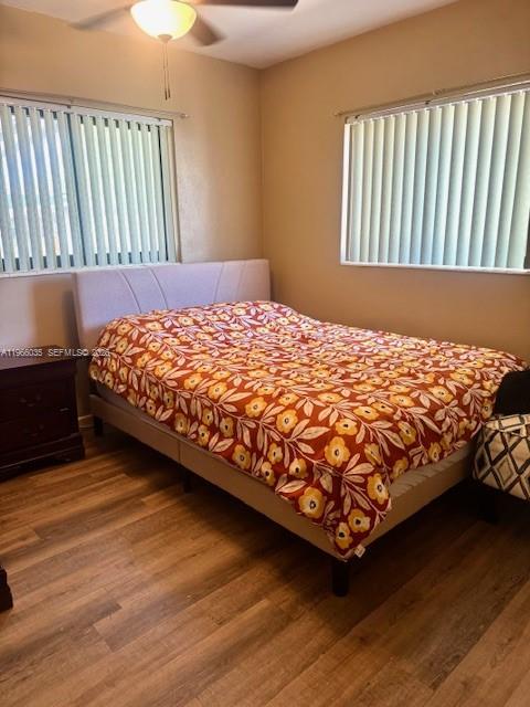 A bedroom features a bed with a floral quilt, wood-look flooring, and two windows — 1481 SW 7th Ter, Deerfield Beach FL 33441, DEERFIELD BEACH, FL