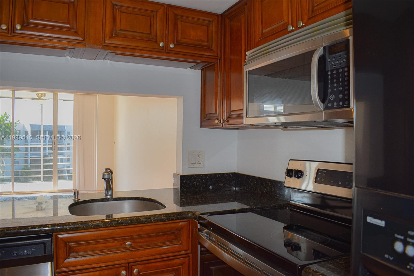 A kitchen features wood cabinets, dark granite countertops, stainless steel appliances, and a pass-through window — 9230 Lagoon Pl # 411, Davie FL 33324, DAVIE, FL