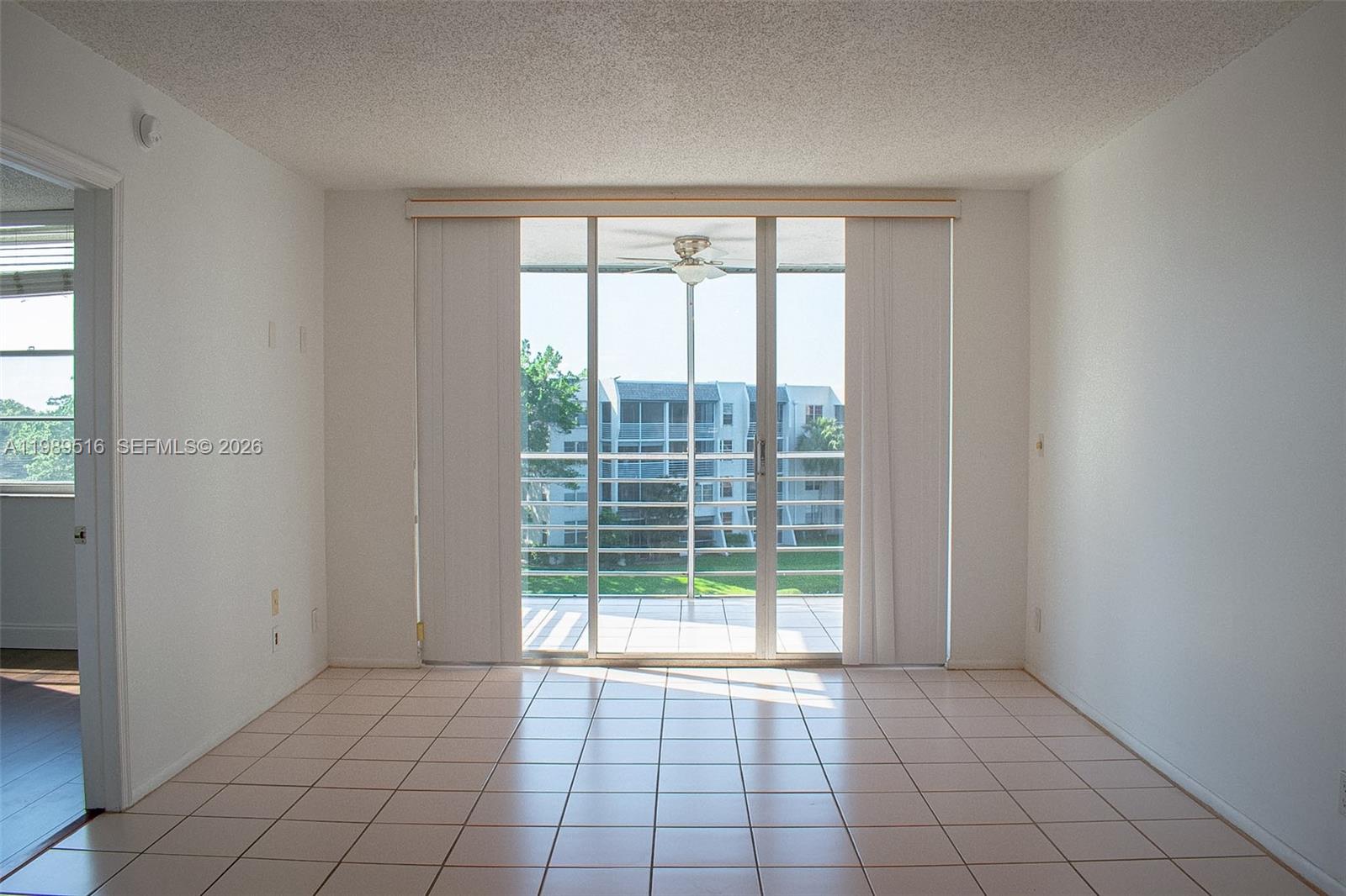 An empty room with light-colored tile flooring features a sliding glass door leading to a balcony — 9230 Lagoon Pl # 411, Davie FL 33324, DAVIE, FL