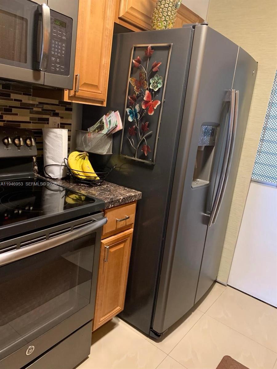 A kitchen features a dark refrigerator, a black stove, wooden cabinets, and a tile backsplash — 16801 NE 13th Ave # 301, Miami FL 33162, MIAMI, FL