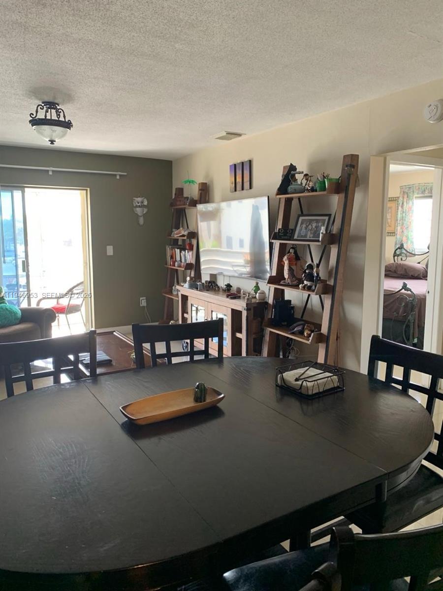 A dining area with a dark round table overlooks a living room with a television — 16801 NE 13th Ave # 301, Miami FL 33162, MIAMI, FL