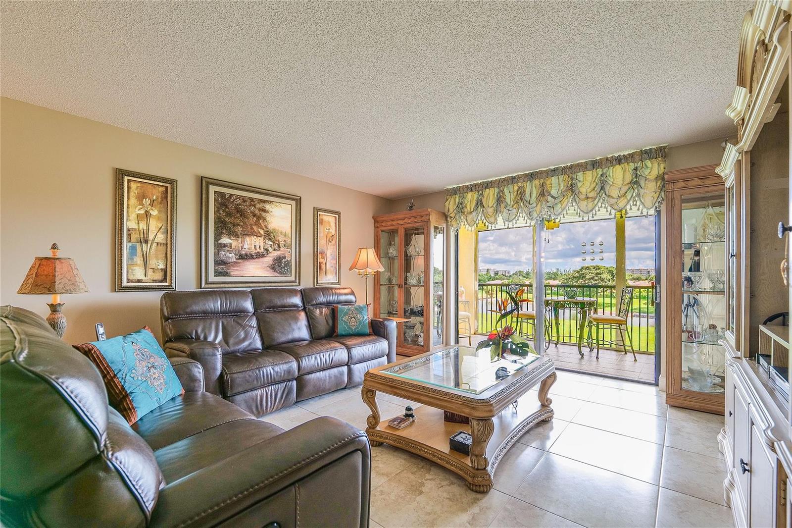 A living room with brown leather sofas, a glass coffee table, and a balcony view — 3650 Environ Boulevard # 401, Lauderhill FL 33319, LAUDERHILL, FL