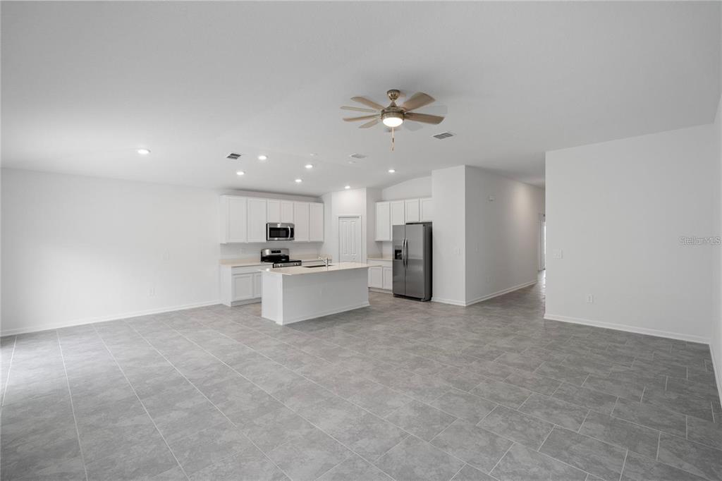 A kitchen with white cabinets and a center island opens into a large tiled room — 4819 WORCHESTER DRIVE, KISSIMMEE, FL