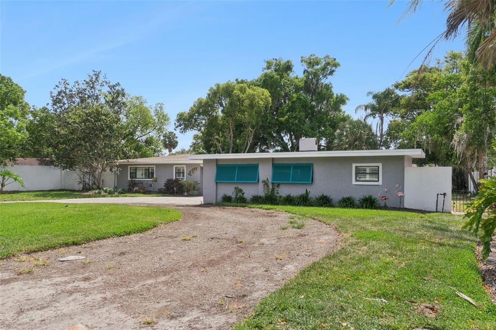 A single-story gray house with turquoise shutters and a dirt driveway under a blue sky — 140 WIGWAM PLACE, MAITLAND, FL