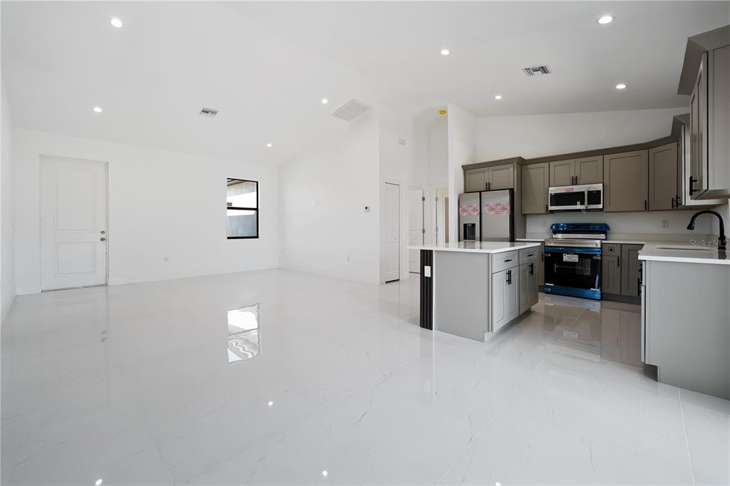 A modern kitchen with gray cabinets and a white island opens into a spacious room — 2458 NW 9TH TERRACE, CAPE CORAL, FL