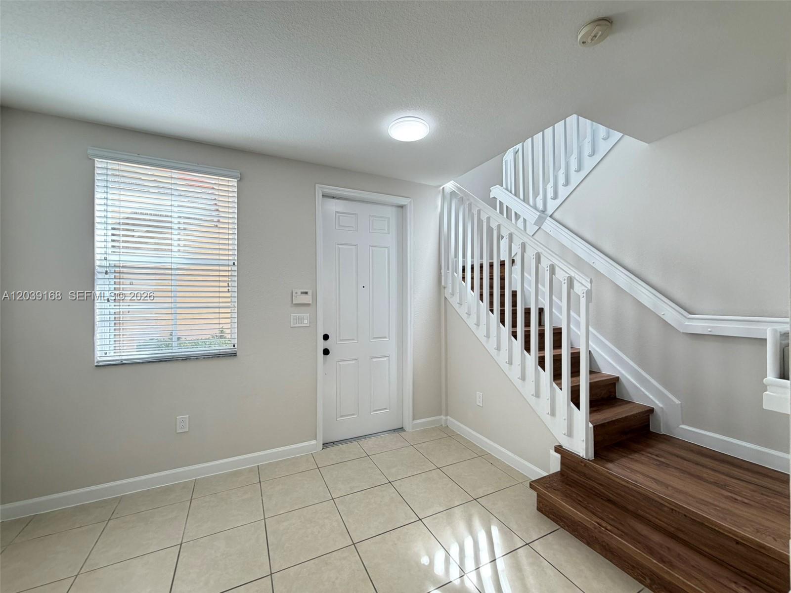 An entryway features light-colored floor tiles, a white front door, and a wooden staircase — 1720 NE 33rd Ave # 5, Homestead FL 33033, HOMESTEAD, FL