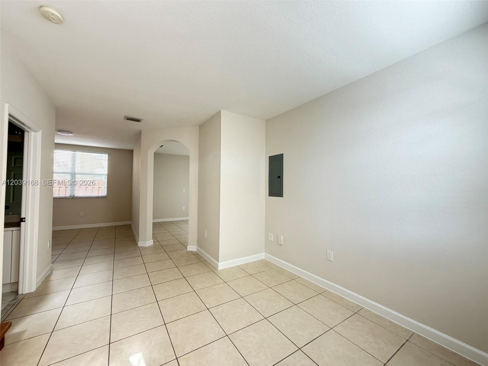 An empty room with beige tile flooring, light-colored walls, and an arched doorway — 1720 NE 33rd Ave # 5, Homestead FL 33033, HOMESTEAD, FL