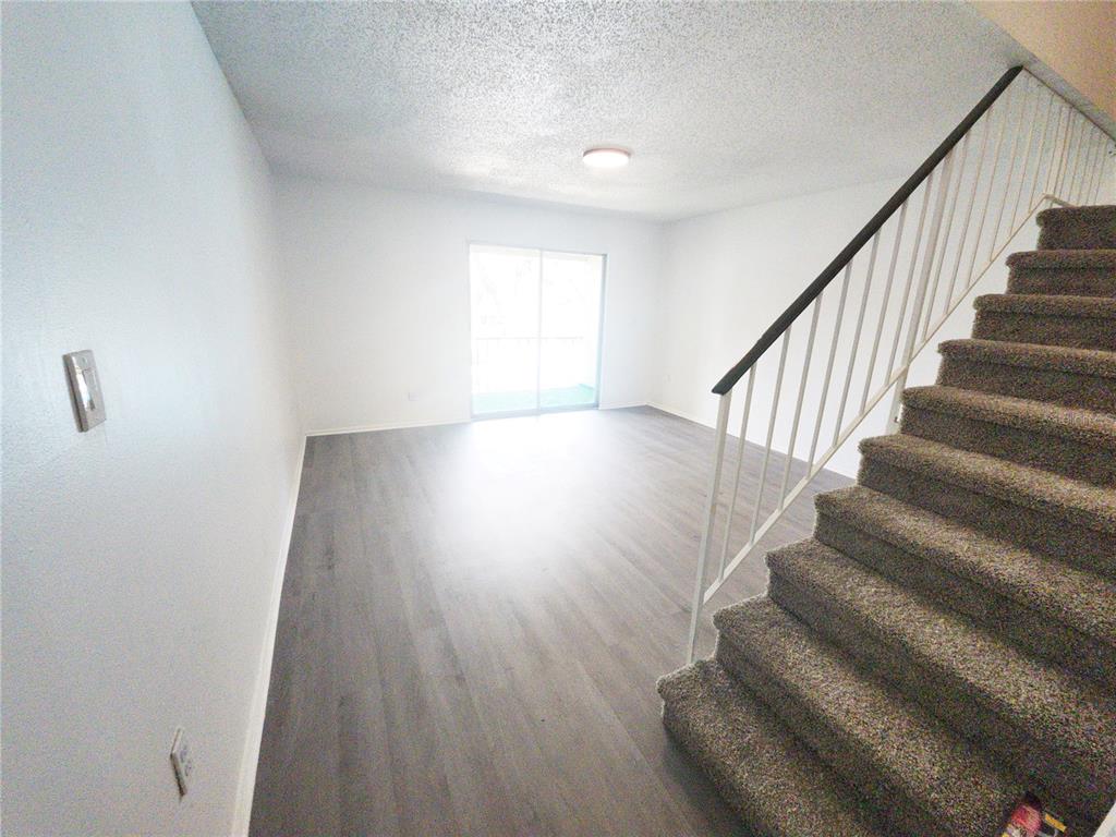 A living room with gray wood-look flooring, white walls, and carpeted stairs with a railing — 14422 REUTER STRASSE CIRCLE UNIT 112, TAMPA, FL