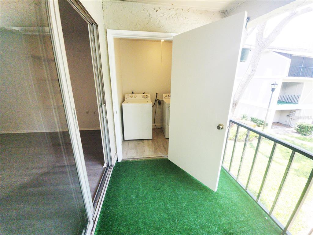 A balcony with green artificial turf features an open door leading to a laundry closet — 14422 REUTER STRASSE CIRCLE UNIT 112, TAMPA, FL