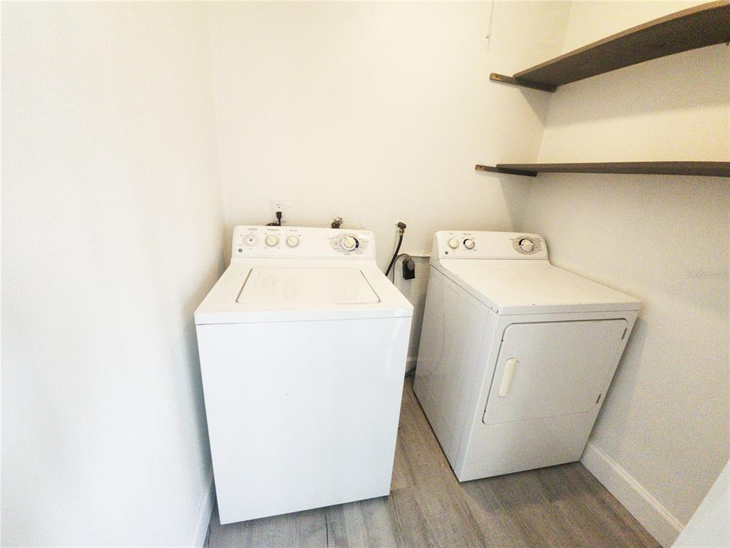 A laundry room features a white washer and dryer with two wooden wall-mounted shelves — 14422 REUTER STRASSE CIRCLE UNIT 112, TAMPA, FL