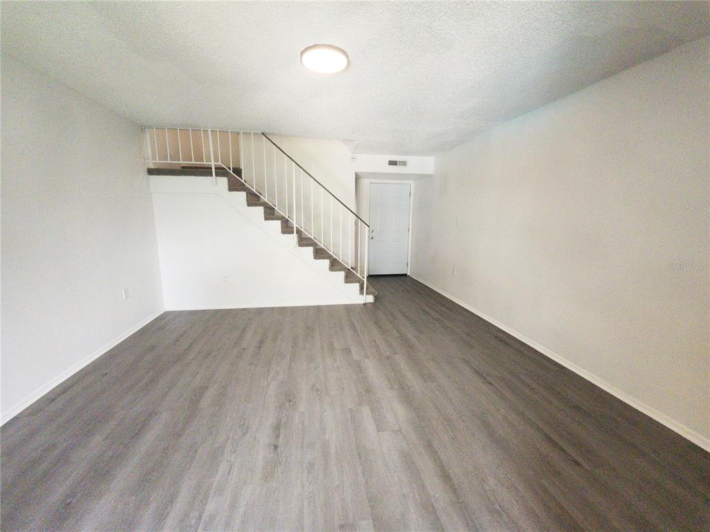An empty living room features gray wood-look flooring, white walls, and a staircase with white railings — 14422 REUTER STRASSE CIRCLE UNIT 112, TAMPA, FL