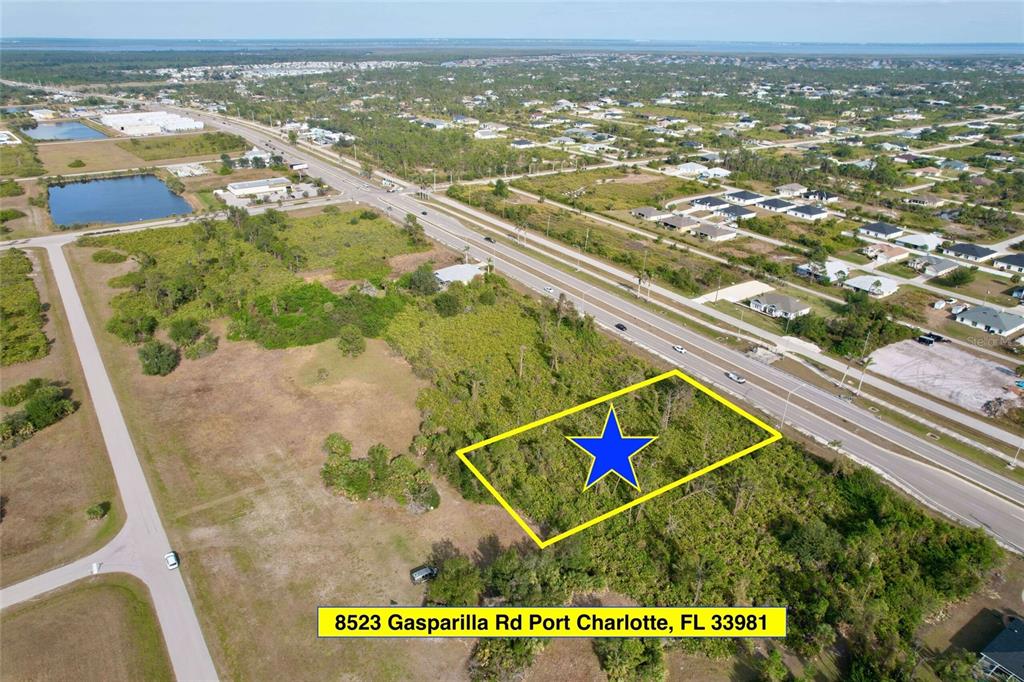An aerial view shows a rectangular, undeveloped lot outlined in yellow next to a highway — 8523 GASPARILLA ROAD, PORT CHARLOTTE, FL