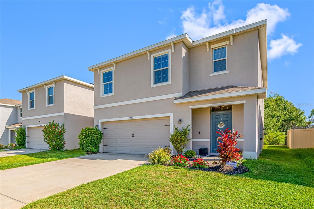 A two-story suburban house with a beige stucco exterior, a two-car garage, and a lawn — 16826 SECRET MEADOW DRIVE, ODESSA, FL