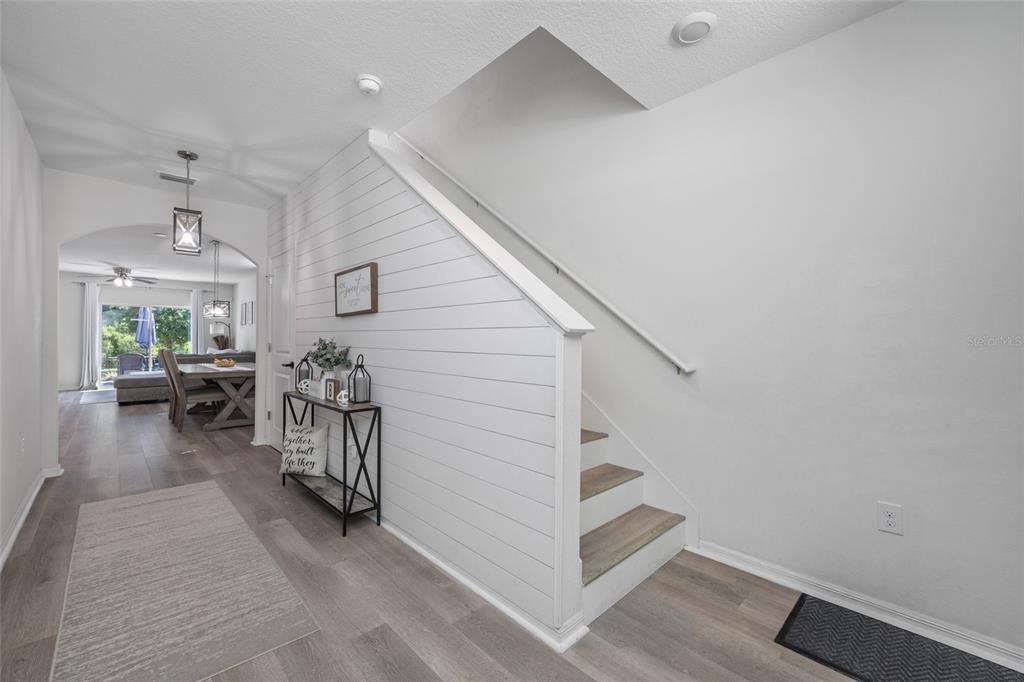 A hallway features a white shiplap staircase, wood-look flooring, and a view into the dining area — 16826 SECRET MEADOW DRIVE, ODESSA, FL