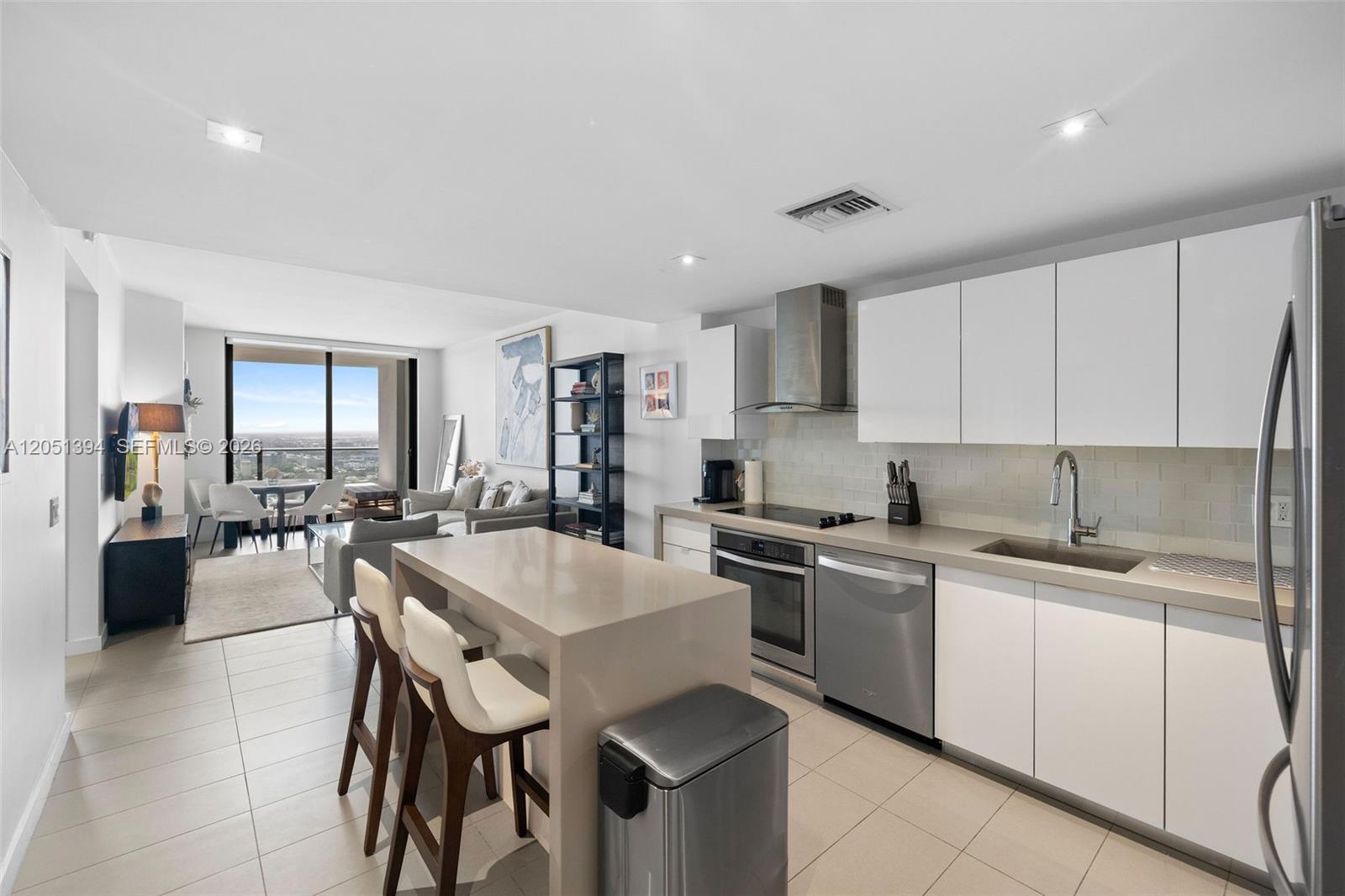 A modern kitchen with white cabinets and a quartz island opens into a living area — 1600 NE 1st Ave # 3111, Miami FL 33132, MIAMI, FL