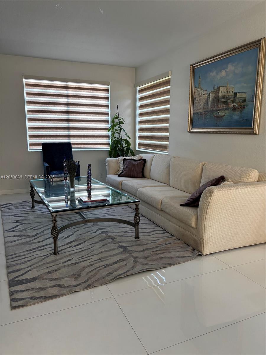A living room features a beige sofa, glass coffee table, patterned rug, and two windows — WESTON, FL