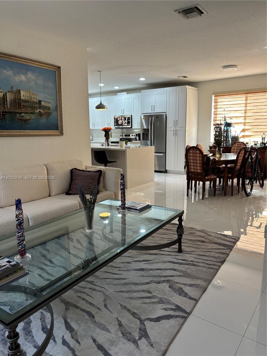 A living room with a glass coffee table opens into a kitchen with white cabinetry — WESTON, FL