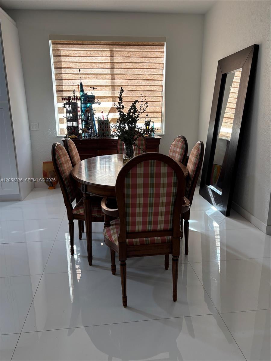A dining room features a round wooden table, plaid chairs, a large mirror, and tiled floors — WESTON, FL