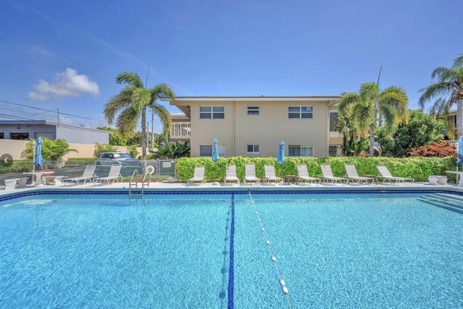 A swimming pool with lounge chairs sits in front of a two-story apartment building — 2121 NE 42ND Court # 202C, Lighthouse Point FL 33064, LIGHTHOUSE POINT, FL