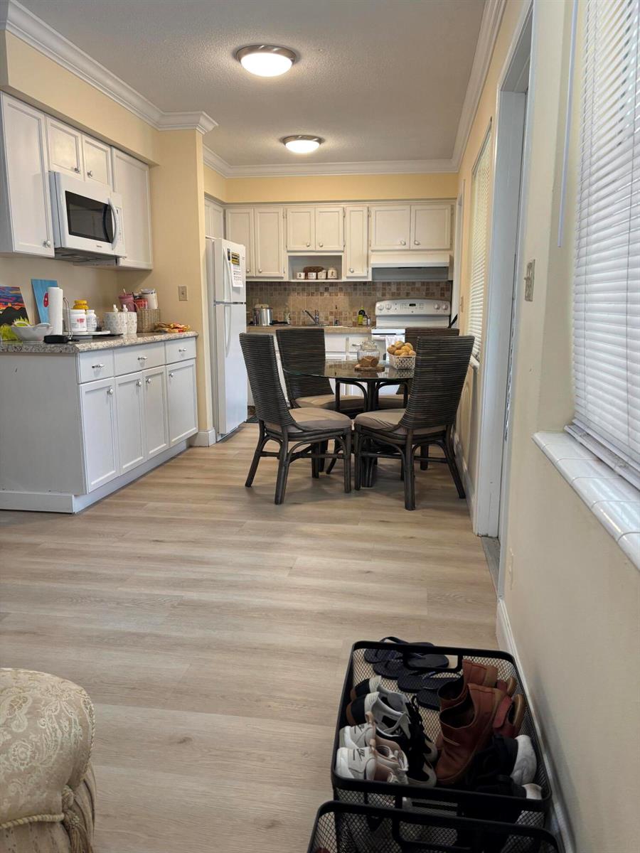A kitchen with white cabinets, light wood-look flooring, and a small dining table with chairs — 2121 NE 42ND Court # 202C, Lighthouse Point FL 33064, LIGHTHOUSE POINT, FL