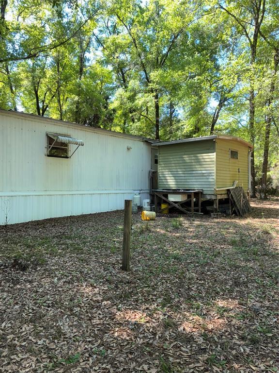 A mobile home exterior with an attached shed and a wooden post in the yard — 24533 PINK PANTHER ROAD, PAISLEY, FL