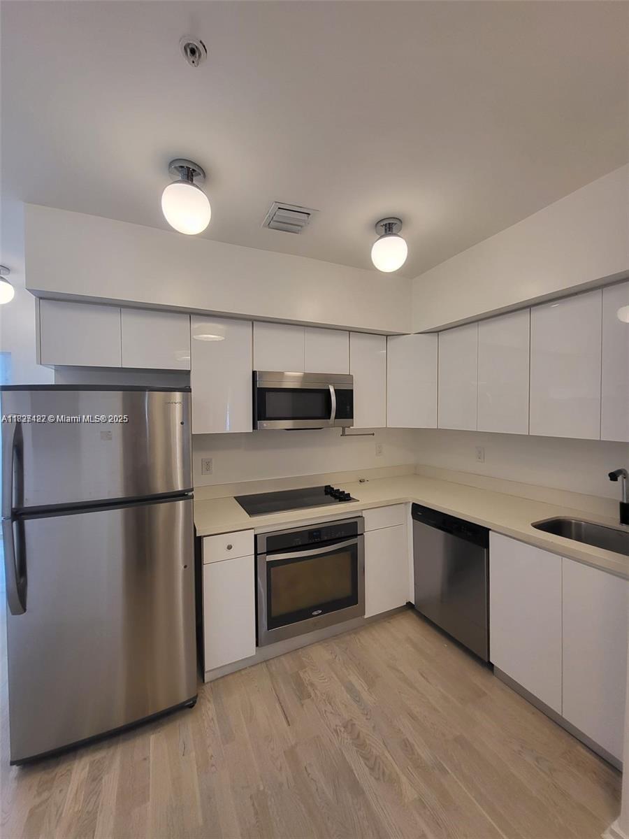 A kitchen features white flat-panel cabinets, stainless steel appliances, and light wood-look flooring — 810 7th St # 206, Miami Beach FL 33139, MIAMI BEACH, FL