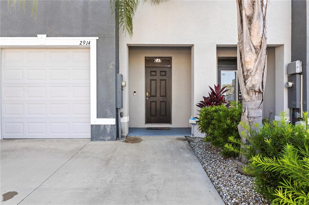 The exterior of a townhouse features a white garage door, a dark front door, and landscaping — 2914 SUNCOAST BLEND DRIVE, ODESSA, FL