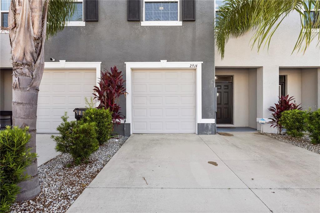 A two-story townhouse exterior features two garage doors, a front entrance, and landscaping — 2914 SUNCOAST BLEND DRIVE, ODESSA, FL