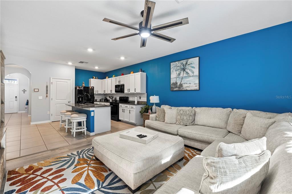 An open-concept living room features a blue accent wall, white kitchen cabinets, and a sectional — 2914 SUNCOAST BLEND DRIVE, ODESSA, FL
