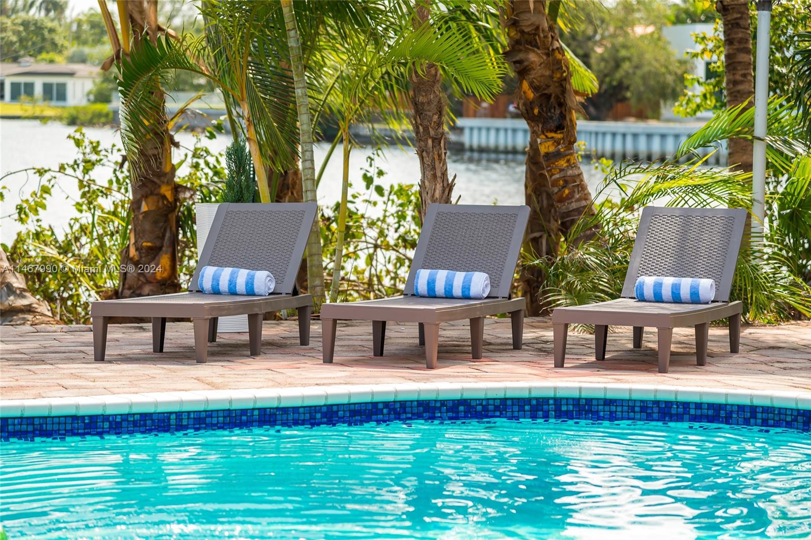 Three lounge chairs with blue and white striped towels sit beside a swimming pool — 2500 NE 199th St, Miami FL 33180, MIAMI, FL
