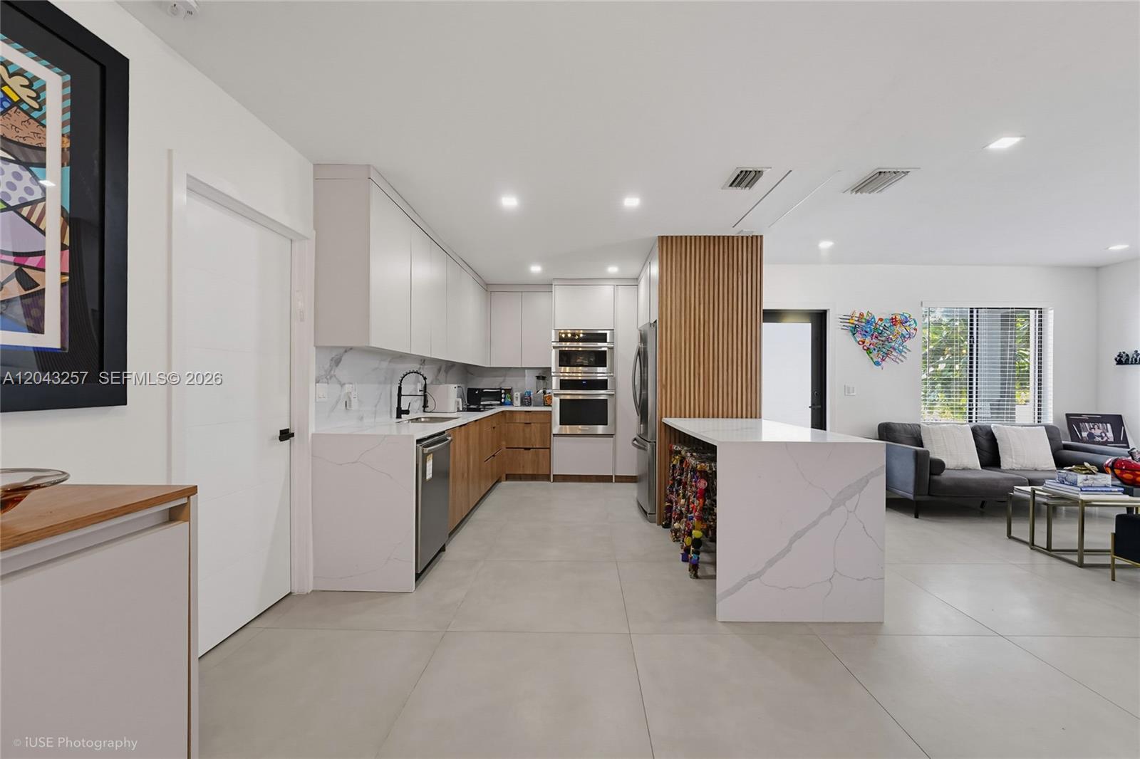 A modern kitchen features white cabinets, wood-toned lower drawers, marble-patterned countertops, and a waterfall island — 2450 NE 209th Ter, Miami FL 33180, MIAMI, FL