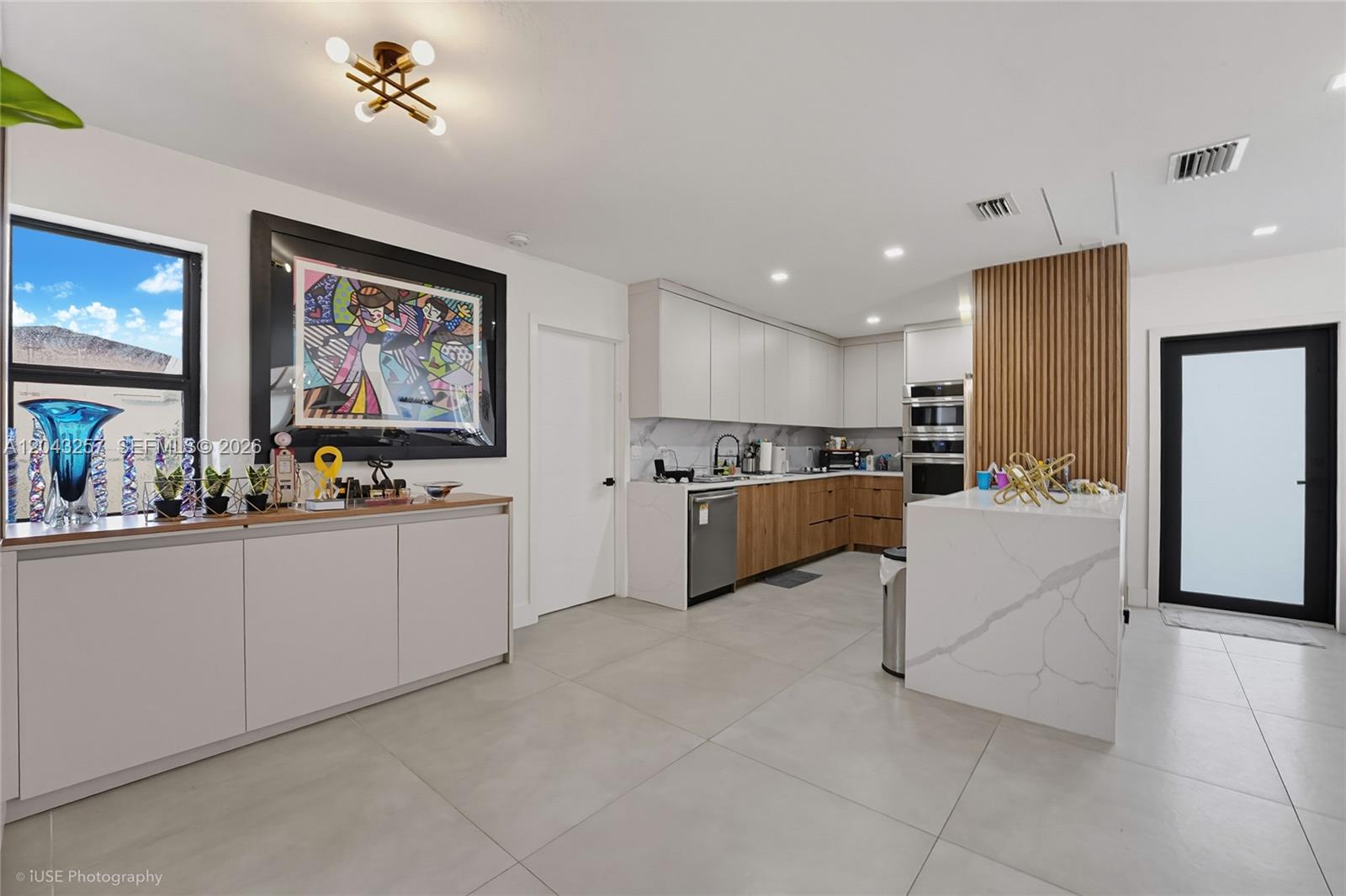 A modern kitchen features white and wood cabinetry, a marble-topped island, and large floor tiles — 2450 NE 209th Ter, Miami FL 33180, MIAMI, FL