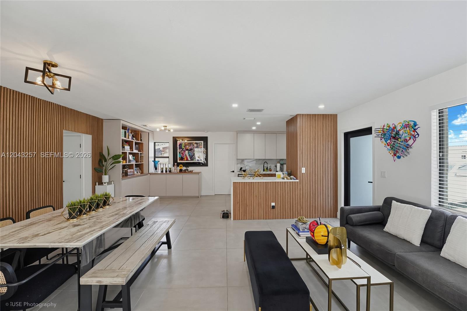 An open-concept living and dining area features wood slat wall accents and light tile flooring — 2450 NE 209th Ter, Miami FL 33180, MIAMI, FL