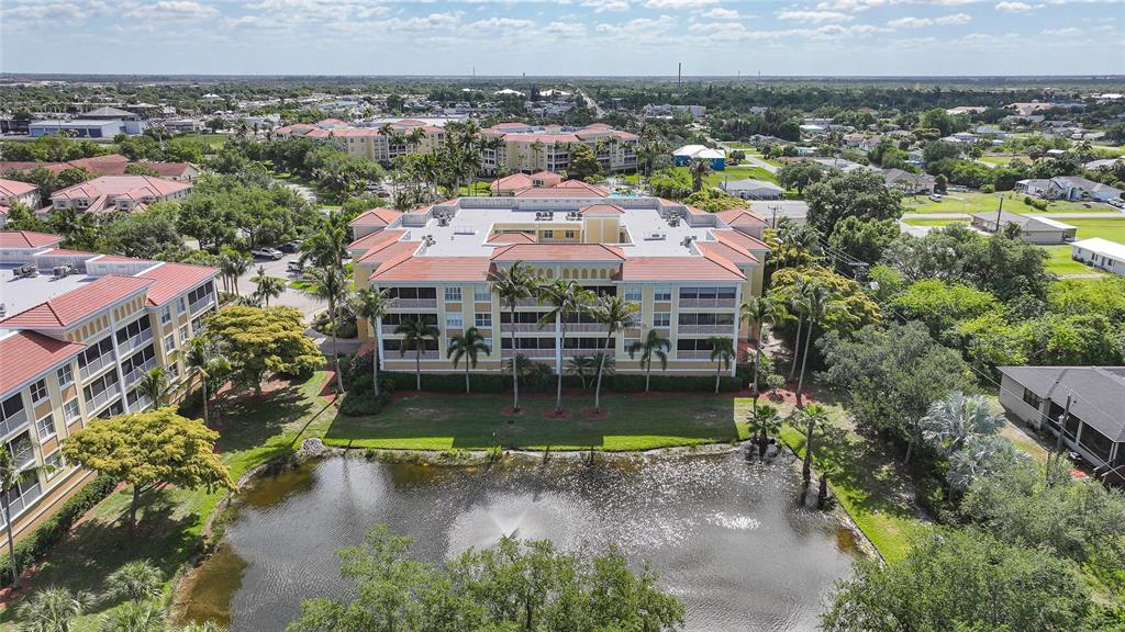 An aerial view shows a multi-story apartment building with a red roof beside a pond — 255 W END DRIVE UNIT 3306, PUNTA GORDA, FL