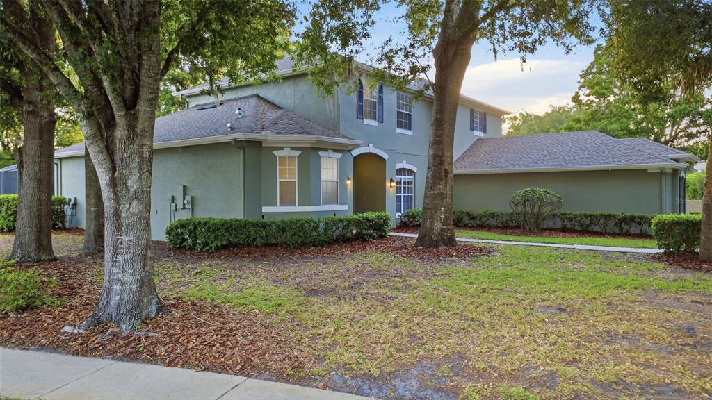 A two-story house with green stucco siding, a shingled roof, and mature trees in front — 1545 CHERRY RIDGE DRIVE, LAKE MARY, FL