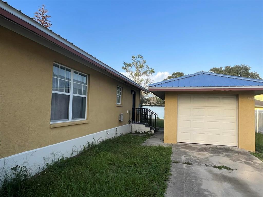 A yellow house with a detached garage and a concrete driveway under a blue roof — 1155 N FLORENCE AVENUE, LAKELAND, FL