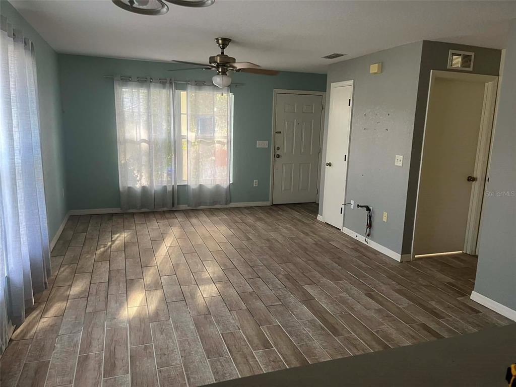 A living room features light blue walls, wood-look tile flooring, a ceiling fan, and windows — 1155 N FLORENCE AVENUE, LAKELAND, FL