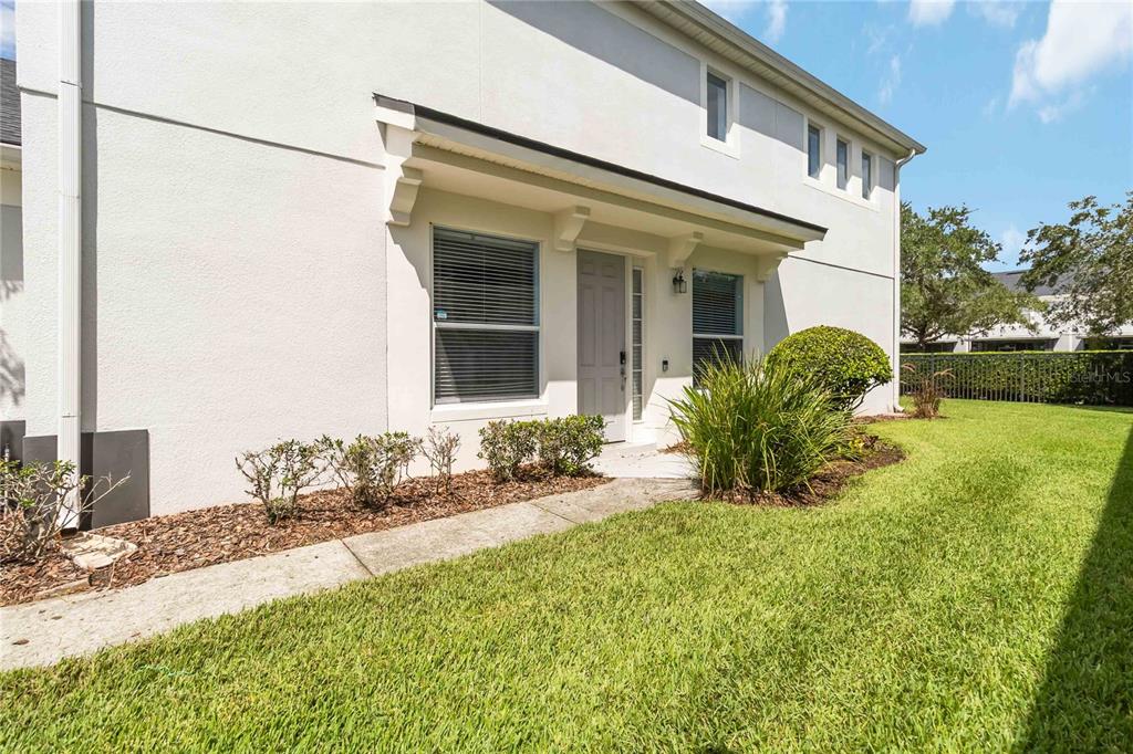A white stucco townhouse exterior features a covered entryway, a walkway, and a grassy lawn — 1706 SHALLCROSS AVENUE, ORLANDO, FL