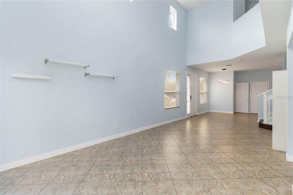 A spacious living room with high ceilings, light blue walls, tile flooring, and wall-mounted shelves — 1706 SHALLCROSS AVENUE, ORLANDO, FL