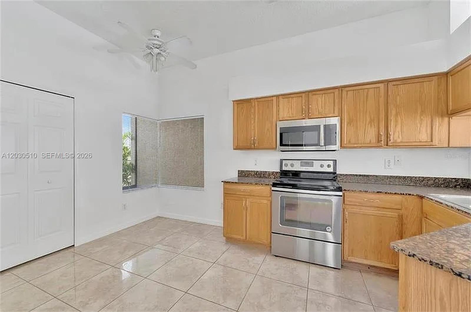 A kitchen features light wood cabinets, stainless steel appliances, granite countertops, and tile flooring — 11007 Whitecap Dr, Riverview FL 33579, RIVERVIEW, FL