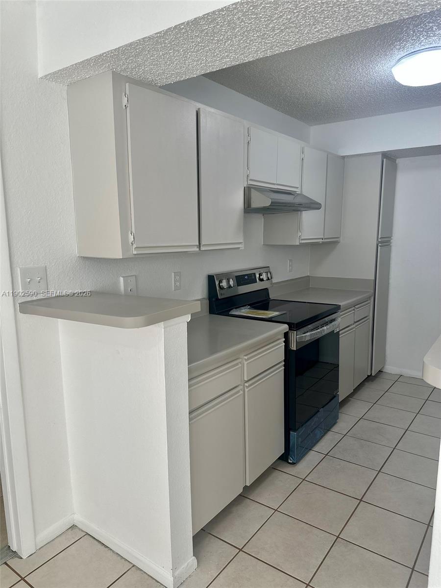 A kitchen features light-colored cabinets, a black stove, and beige countertops with tiled flooring — 10581 SW 155th Ct # 1214, Miami FL 33196, MIAMI, FL