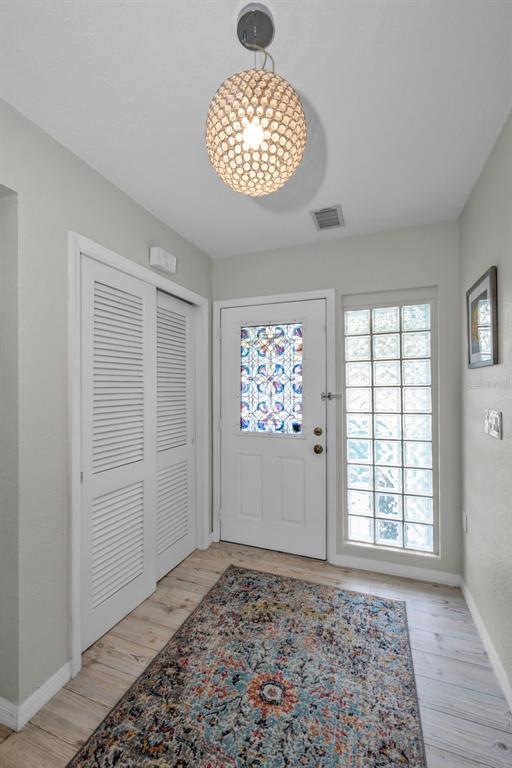 An entryway features a patterned rug, a crystal pendant light, louvered closet doors, and a glass-paneled door — 1948 BYRAM DRIVE, CLEARWATER, FL