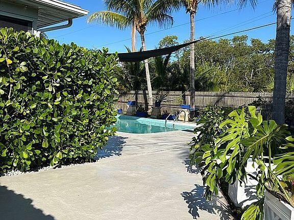A backyard features a swimming pool, a concrete patio, a large hedge, and palm trees — 186 12th Street SE, Vero Beach FL 32962, VERO BEACH, FL