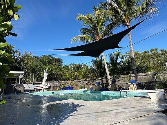 A backyard swimming pool features a black shade sail, palm trees, and a concrete deck — 186 12th Street SE, Vero Beach FL 32962, VERO BEACH, FL