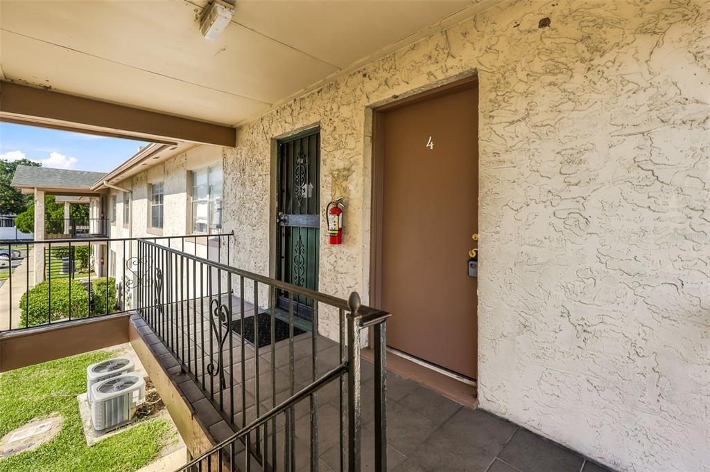 An exterior view of an apartment building walkway featuring a brown door labeled number four — 1910 HONOUR ROAD UNIT 4, ORLANDO, FL