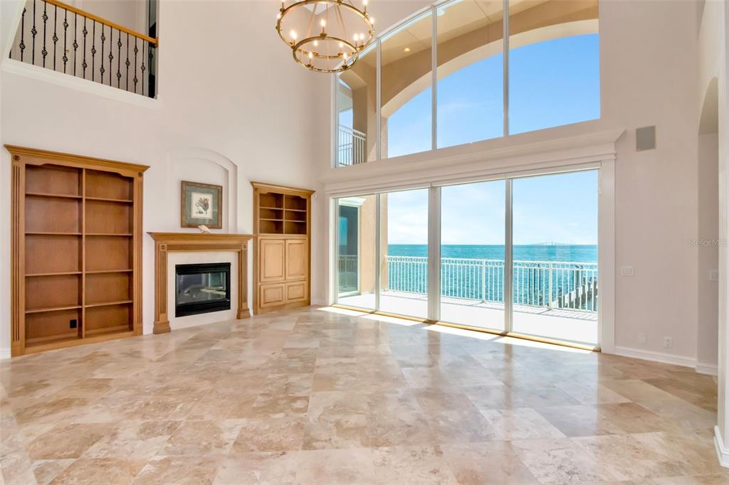 A living room features a fireplace, built-in shelving, tile floors, and floor-to-ceiling windows overlooking water — 7680 PARADISE POINTE CIRCLE S, ST PETERSBURG, FL