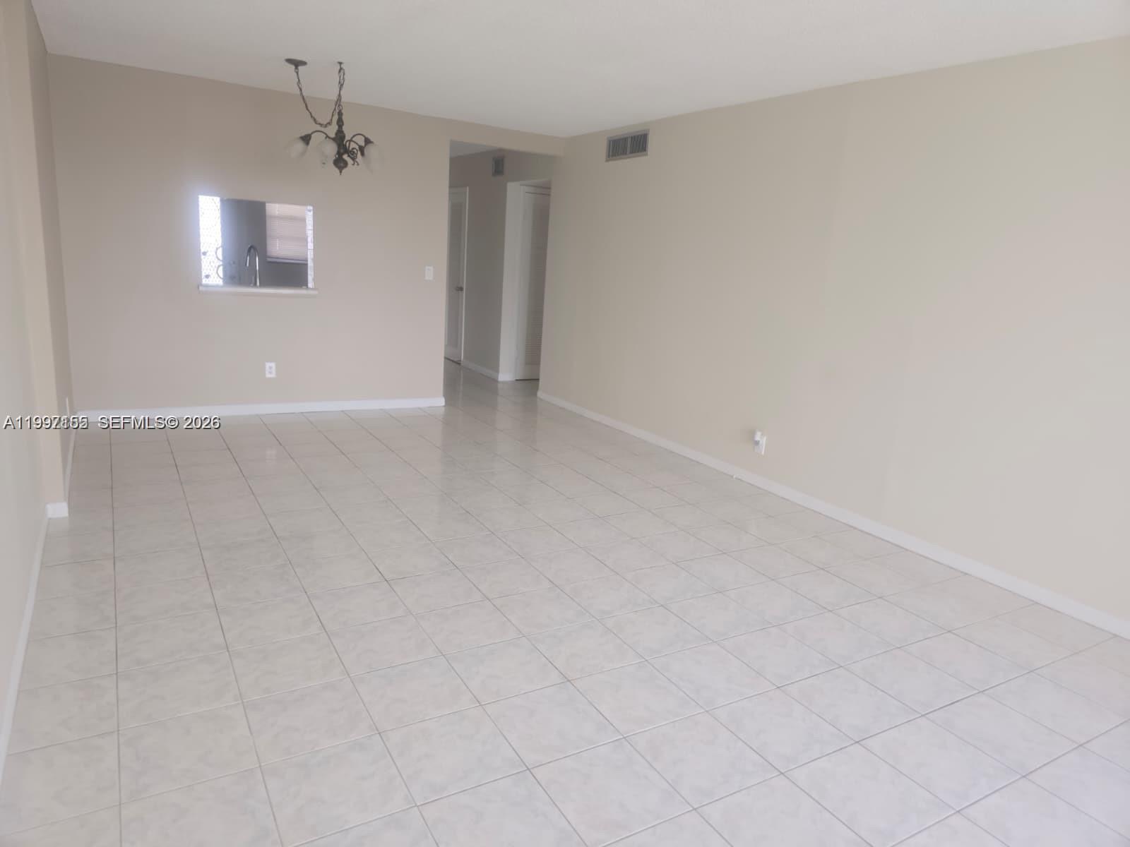 An empty room features light-colored tile flooring, beige walls, and a hanging light fixture — 320 NE 12th Ave # 703, Hallandale Beach FL 33009, HALLANDALE BEACH, FL