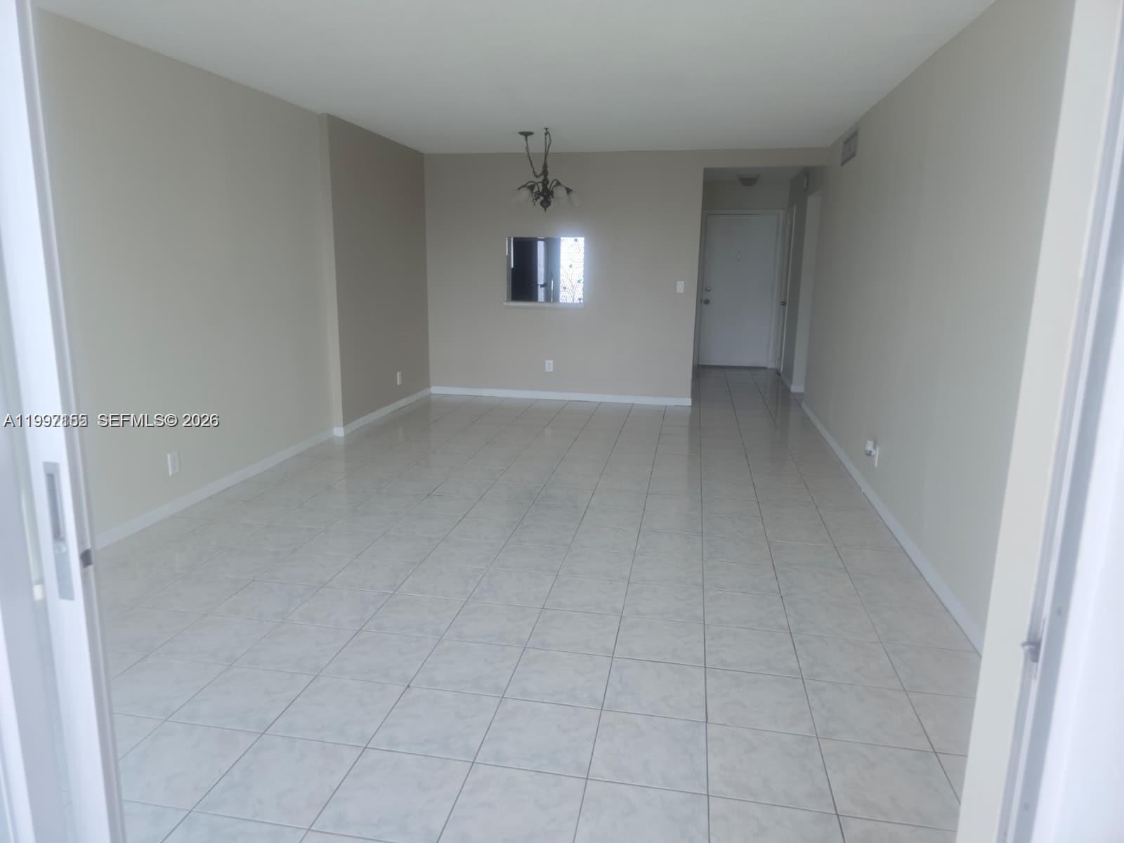 An empty room features light-colored tile flooring, beige walls, and a small pass-through window — 320 NE 12th Ave # 703, Hallandale Beach FL 33009, HALLANDALE BEACH, FL